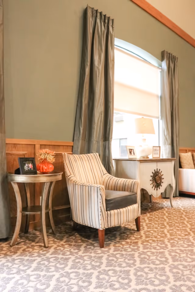 Striped upholstered armchair between side tables and a window with long curtains in a cozy lounge area.
