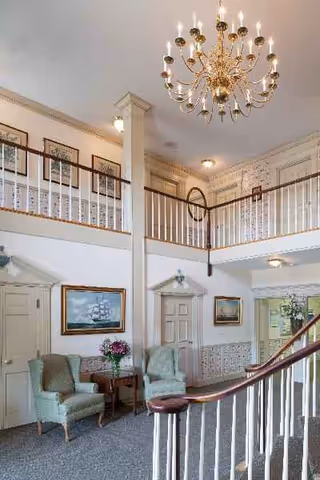 Elegant two-story lobby with chandelier, white railings, and comfy seating near a curved staircase.
