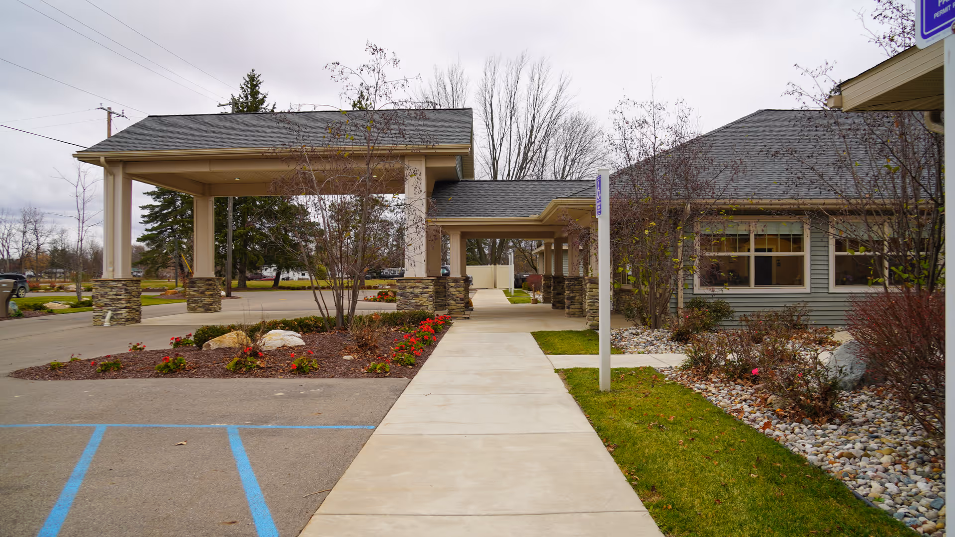 Front entrance with a covered porte-cochère, concrete walkway, and landscaped beds in front of a single-story building.