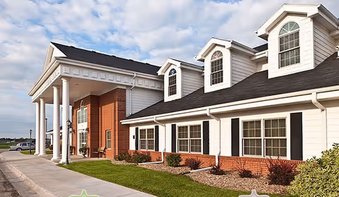 Front exterior of a senior living facility with brick, white siding, columns, and manicured landscaping.
