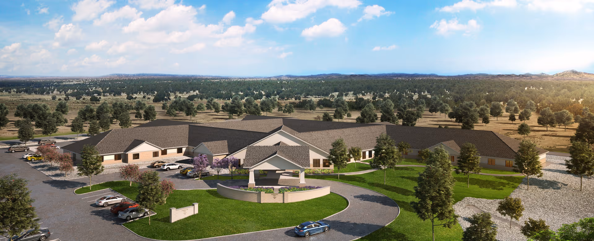 Aerial view of a single-story nursing and transitional care facility named Las Alturas Nursing & Transitional Care, surrounded by landscaped green lawns, trees, and parking areas, set in a wide open natural landscape with distant hills under a partly cloudy sky.