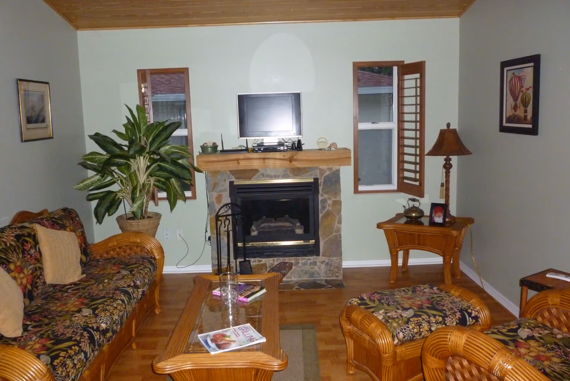 Cozy living room with wicker furniture, a coffee table, a large potted plant, and a stone fireplace with a TV mounted above.