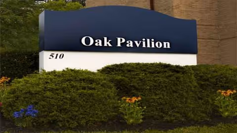 Oak Pavilion sign atop a white base with landscaping in front of a brick building.