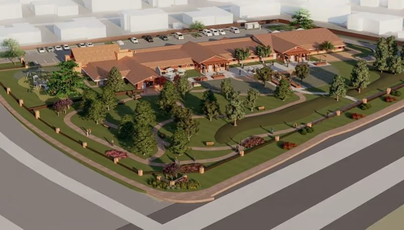 Aerial view of a senior living facility named Open Arms Assisted Living, showing a large building with multiple sections and a red-tiled roof surrounded by landscaped gardens, walking paths, trees, benches, and parking spaces.