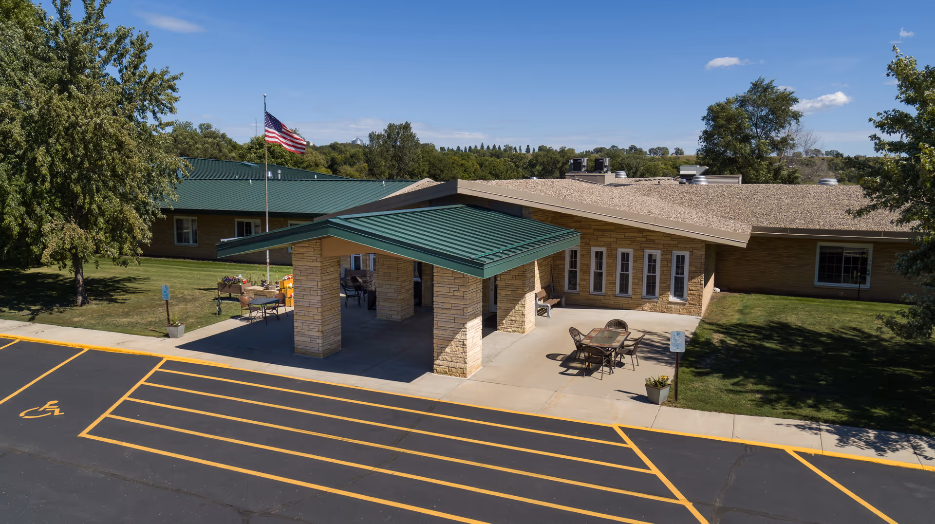 Front entrance of Browns Valley Health Center showing a covered drop-off with green roof, American flag, outdoor seating, and parking markings.