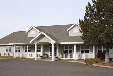 Front view of a single-story senior living building with a covered entrance and parking.
