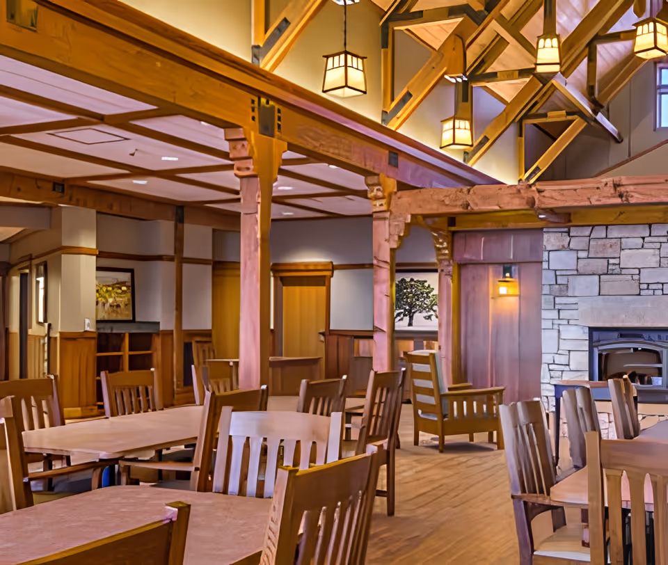 Interior view of the dining room at Mesa View Assisted Living, featuring wooden tables and chairs, a stone fireplace, and decorative lighting.