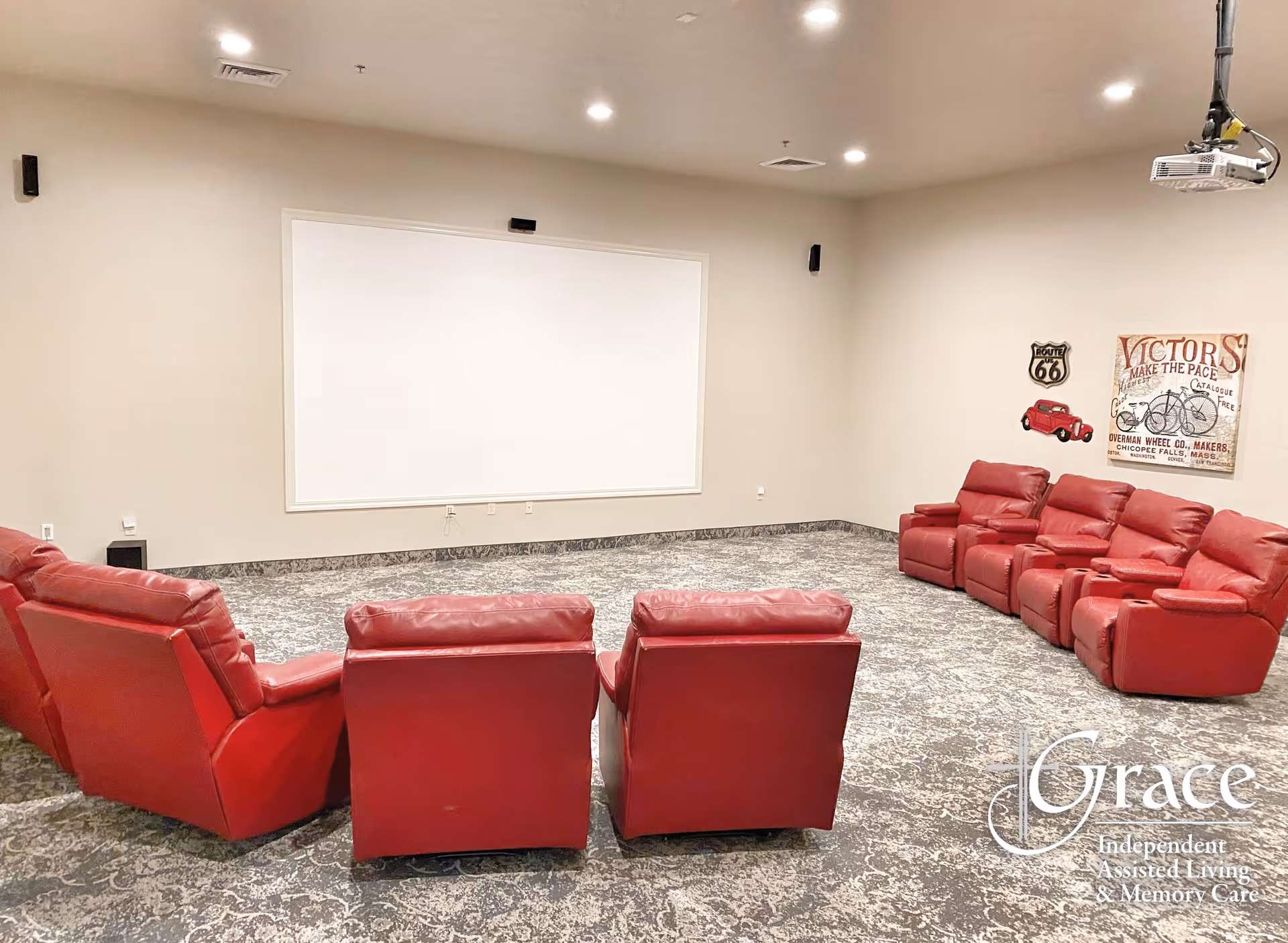 A small theater-style room with red recliner seats arranged facing a large blank projection screen.