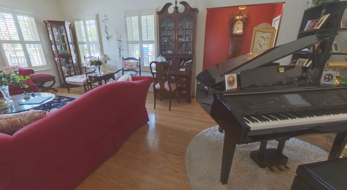 Bright living room with a black grand piano, red sofa, chairs, and wood flooring.