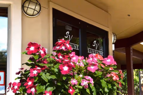 Entrance doors of Sunshine Circle Assisted Living Enclave with bright pink flowers in the foreground and round outdoor wall lights on either side of the doors.