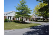 Single-story brick building front with a circular driveway, lawn, and trees under a clear blue sky.