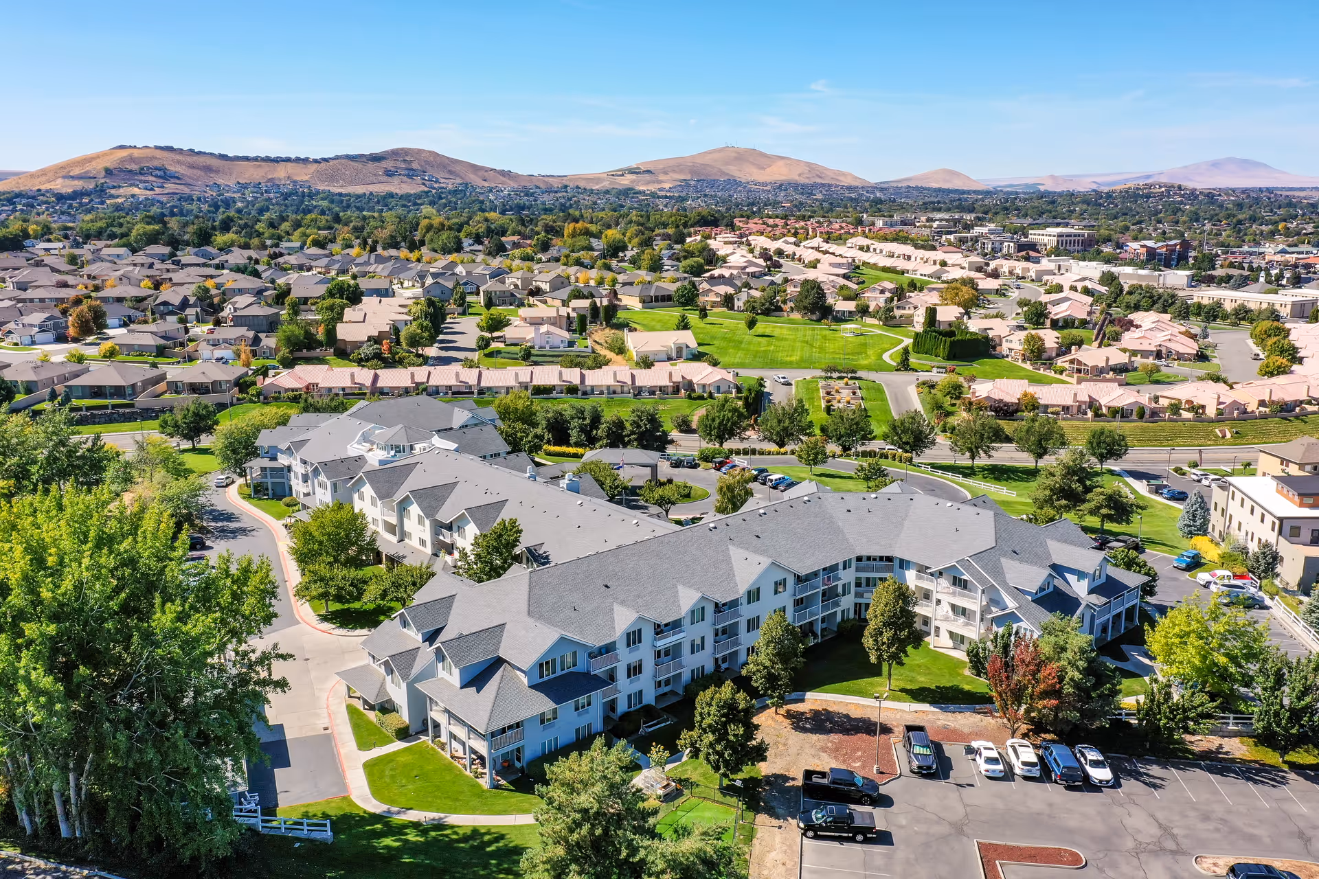 Aerial view of the Solstice Senior Living at Kennewick campus showing multi-story buildings, parking areas, green lawns and the surrounding neighborhood with hills in the distance.