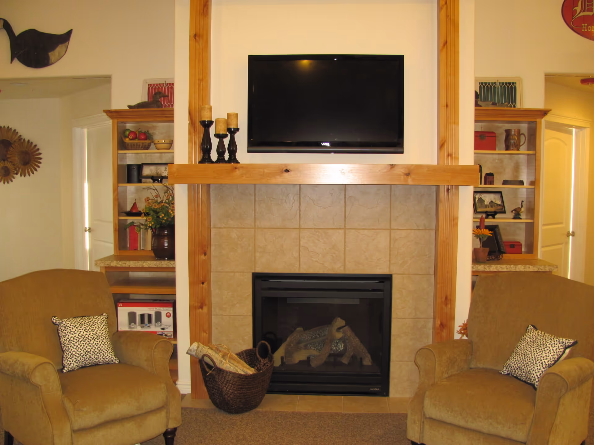 Cozy living room with two armchairs flanking a tiled fireplace topped by a mounted TV and decorative shelving.