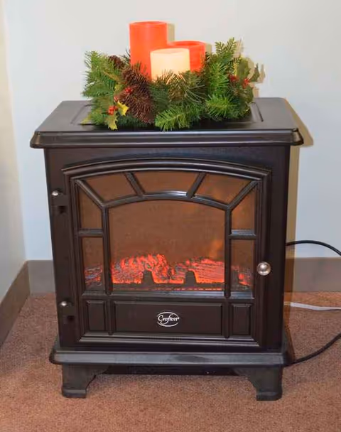 Dark wooden stove with candles and greenery on top sits in a carpeted interior.