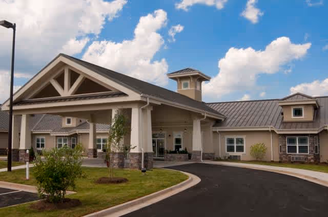Exterior view of Benton House of Covington, showing a single-story building with a covered entrance, beige walls, stone accents, and a metal roof under a partly cloudy sky.