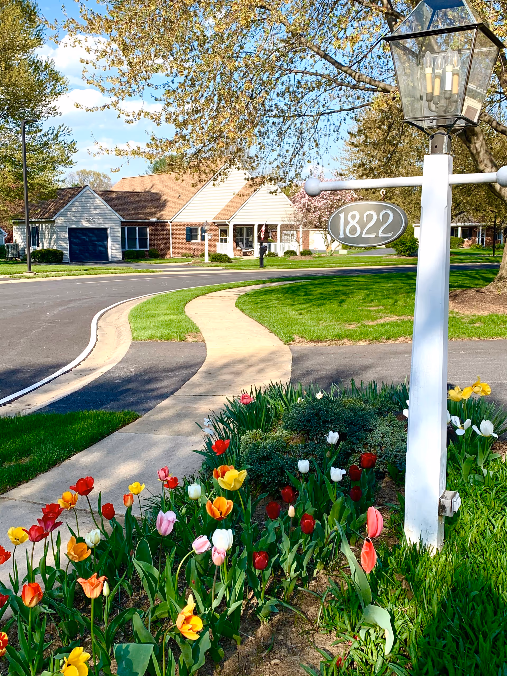 Landscaped front entrance with colorful tulips, a white signpost reading '1822', a curved sidewalk and single-story homes in the background.