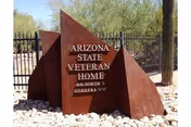 Rust-colored metal sign reads Arizona State Veteran Home beside a gated entrance.