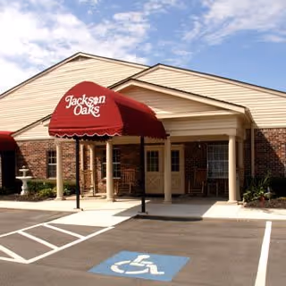 Front entrance of a single-story brick building with a red awning reading 'Jackson Oaks' and a marked handicap parking space.
