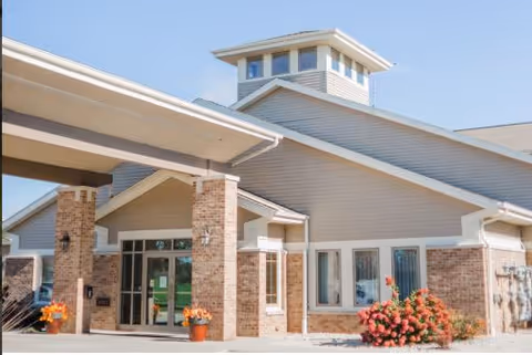 Front entrance of a single-story brick and siding healthcare building with a covered drop-off porte-cochere and potted plants.