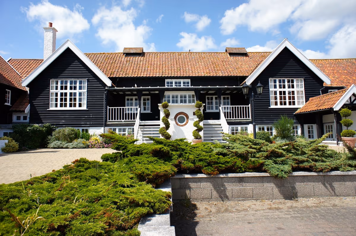 Front exterior of a large two-story black wooden house with a tiled roof, central staircase and landscaped shrubs.