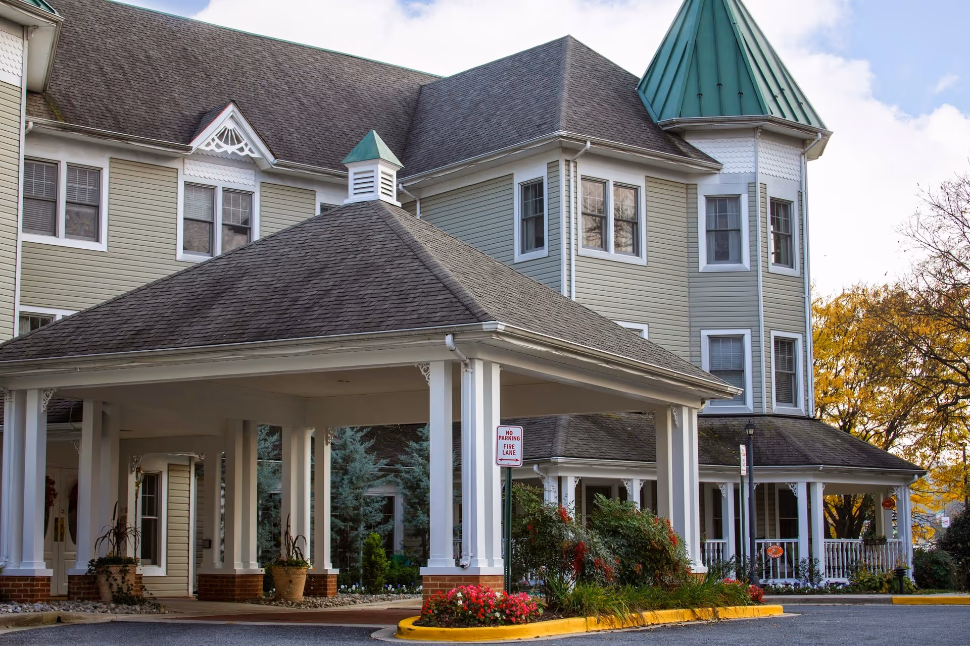 Front entrance of a multi-story senior living facility with a covered porte-cochere and a turreted corner.