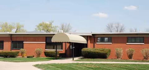 Brick exterior building with an awning-covered entrance and trimmed shrubs.