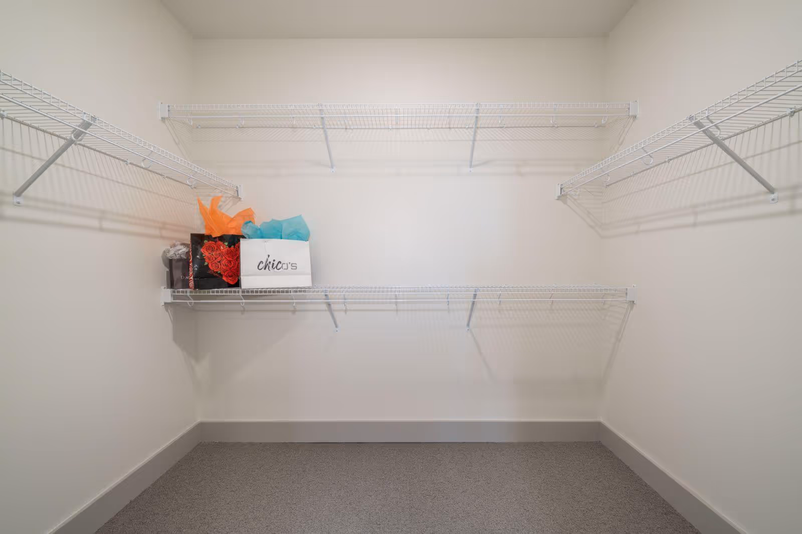 Empty walk-in closet with white wire shelving on three walls and a few shopping bags placed on the left side shelf.