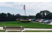 Parking lot with several cars, a flagpole, bench, and manicured green lawn.