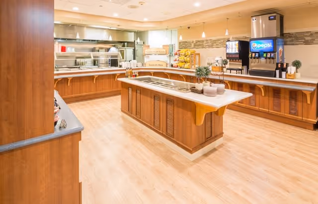 Well-lit dining room buffet area with a central serving island, long service counters and a Pepsi soda dispenser.