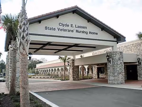 Front entrance of Clyde E. Lassen State Veterans' Nursing Home with stone columns and palm trees.