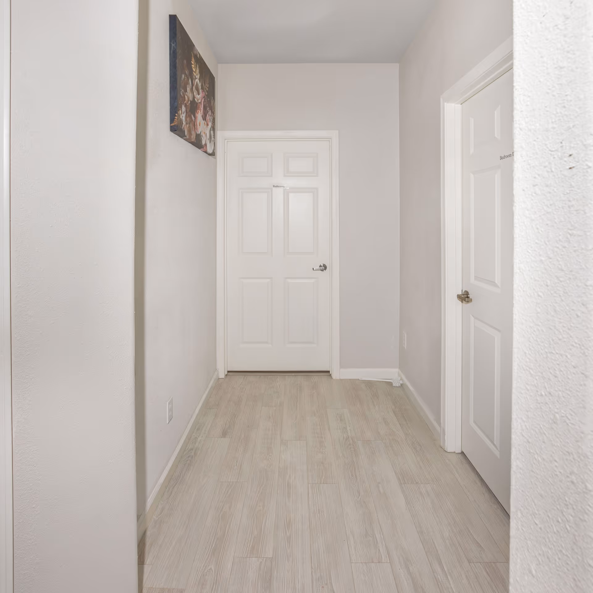 Interior hallway with light walls, doors, and wall art along the corridor.