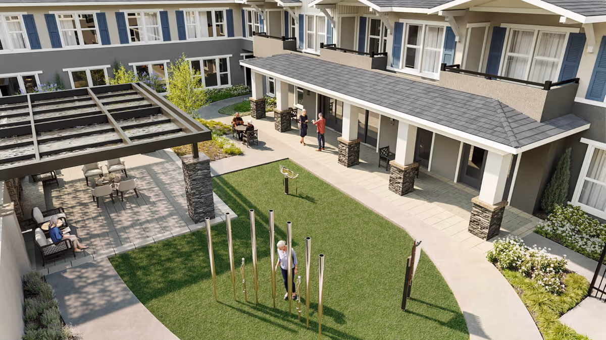 Sunlit courtyard with a grassy lawn, tall chime-like poles, a pergola-covered seating area, and residents walking and sitting near the building.