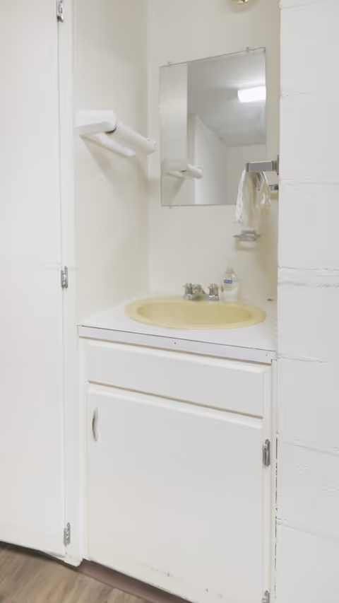A white bathroom vanity with sink, mirror, towel rack, and soap bottle in a small bathroom.