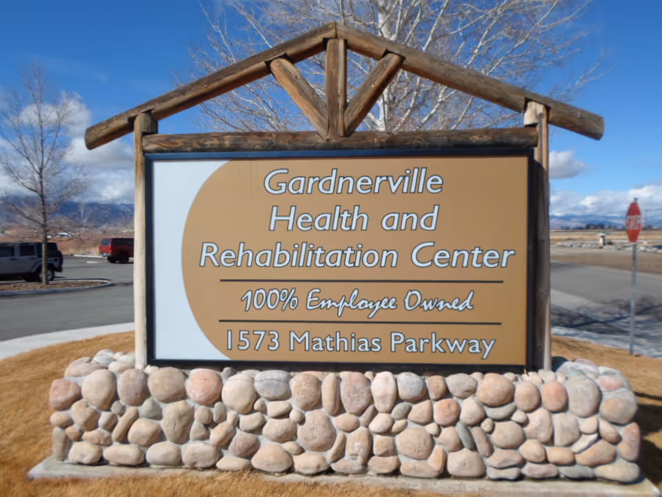Outdoor wooden sign reading "Gardnerville Health and Rehabilitation Center, 1573 Mathias Parkway" mounted on a stone base by the roadside.