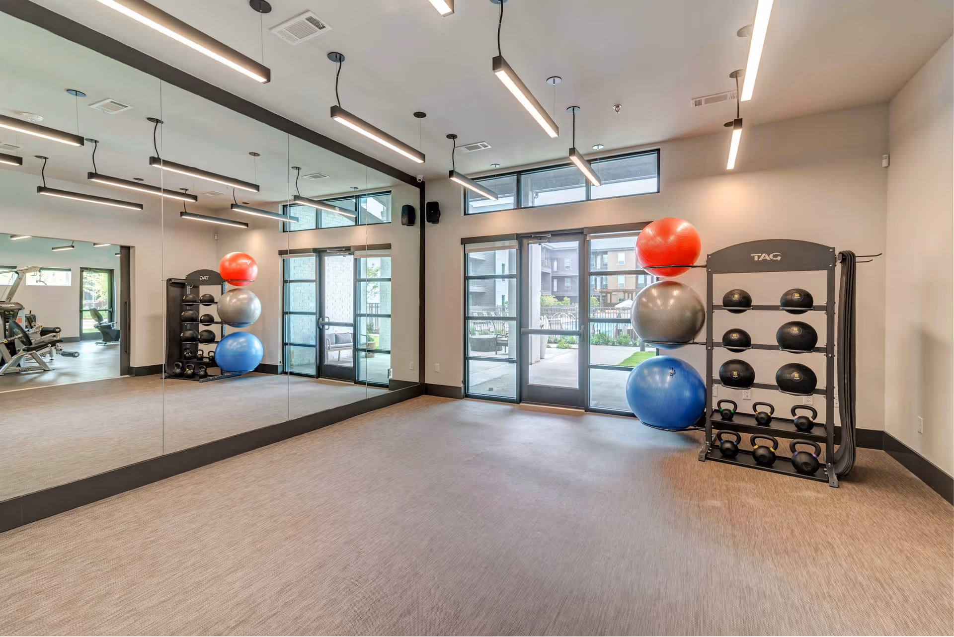 Fitness studio with a mirrored wall, stacked exercise balls, medicine balls and kettlebells near glass doors.