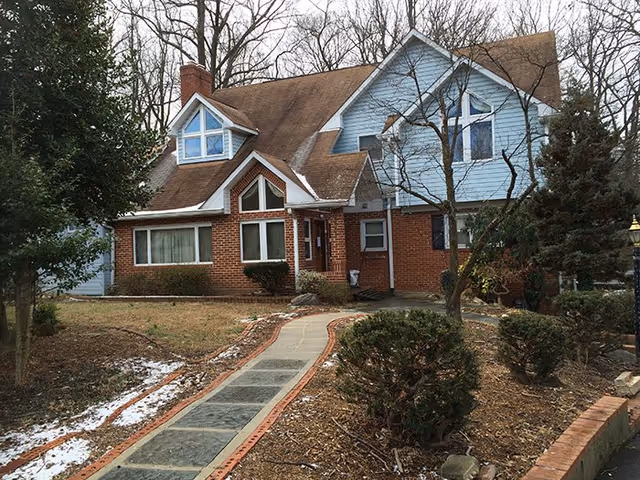 House-style senior living facility with brick base, blue siding, and a brick-edged walkway.