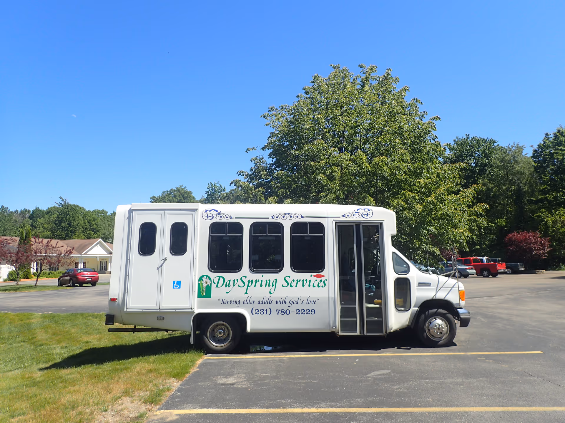 A white DaySpring Services shuttle bus parked in a lot in front of trees under a clear blue sky.