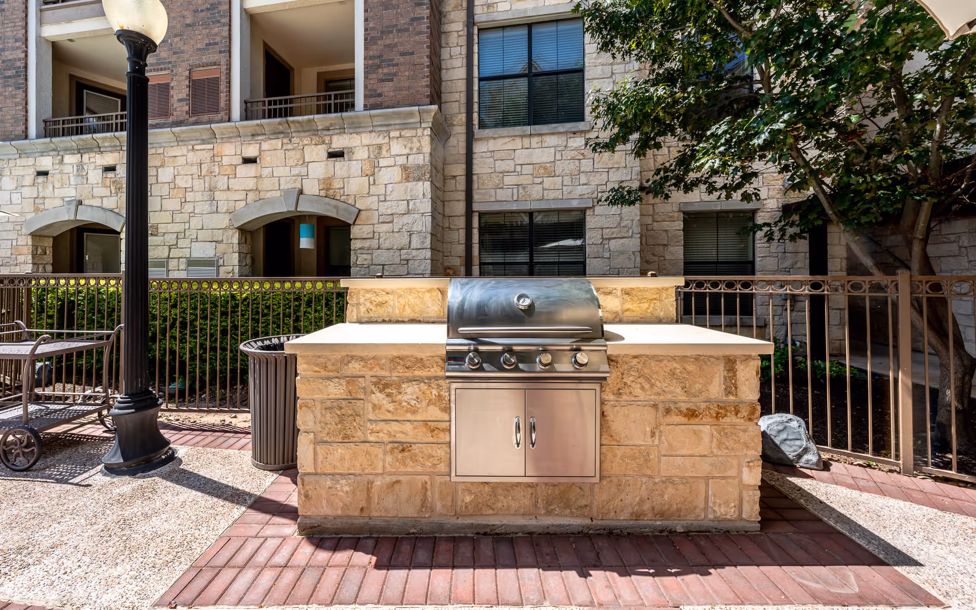 Built-in stainless steel outdoor grill set into a stone countertop on a patio in front of a multi-story stone building.