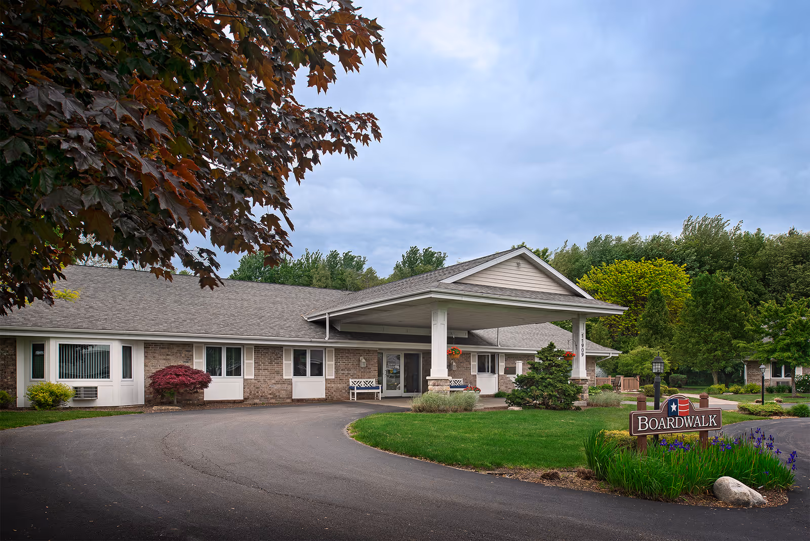 Front exterior of a single-story senior living building with a covered entrance and a 'Boardwalk' sign amid landscaping.