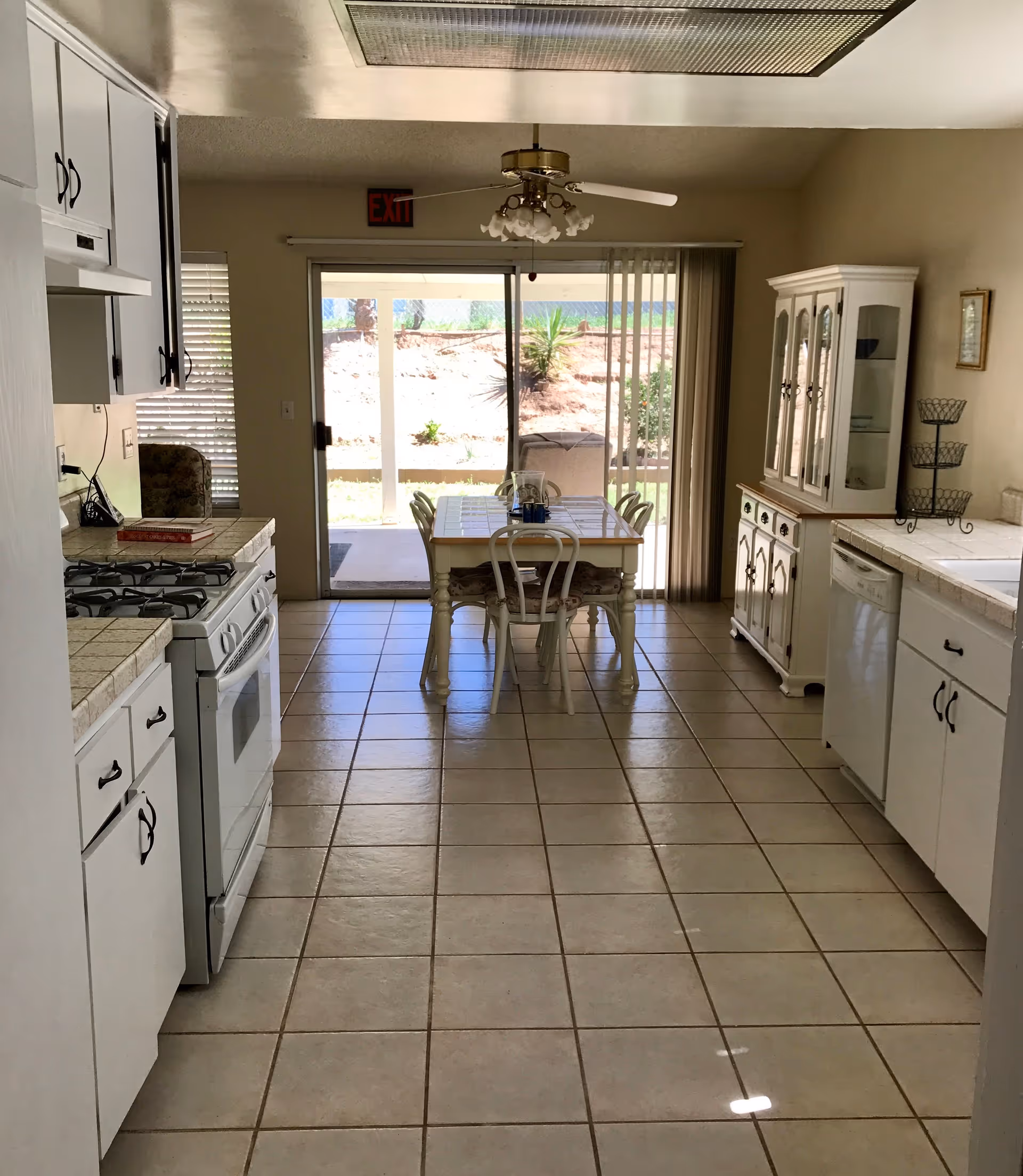 Tiled kitchen with white cabinets and stove leading to a small dining table by sliding glass doors to the backyard.