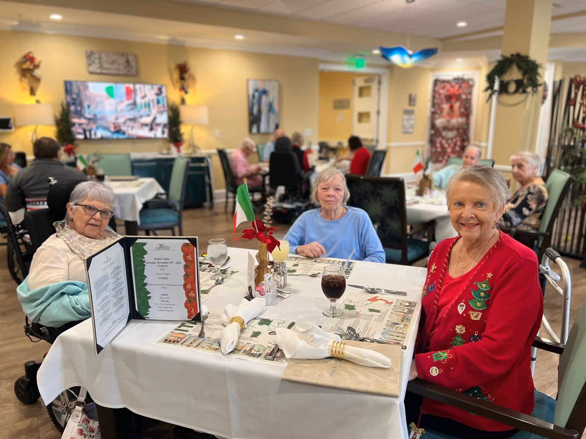 Elderly residents seated around a decorated table enjoying a meal in a communal dining room.