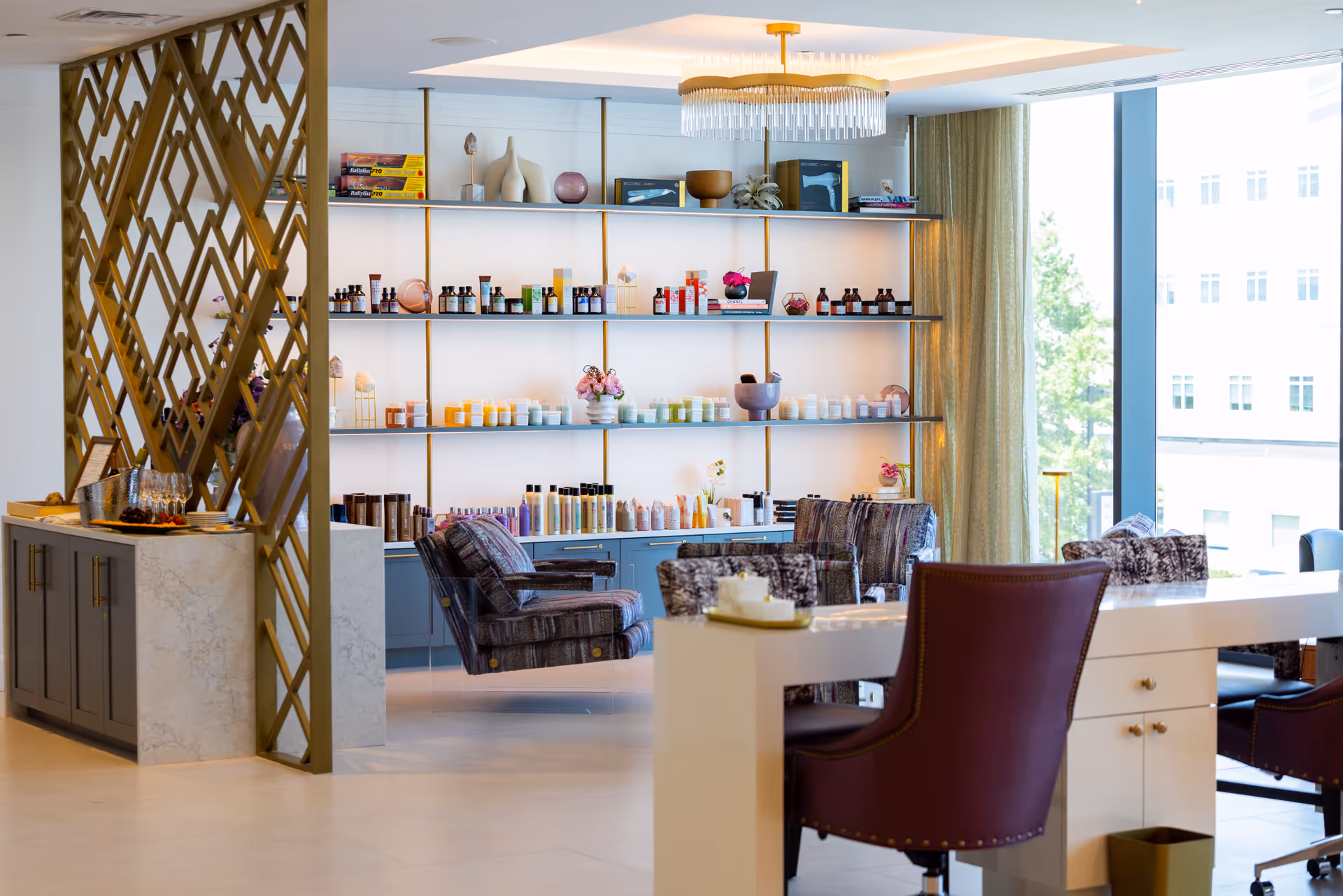 Well-lit interior salon/lounge with shelves of beauty products, armchairs, and manicure stations by large windows.