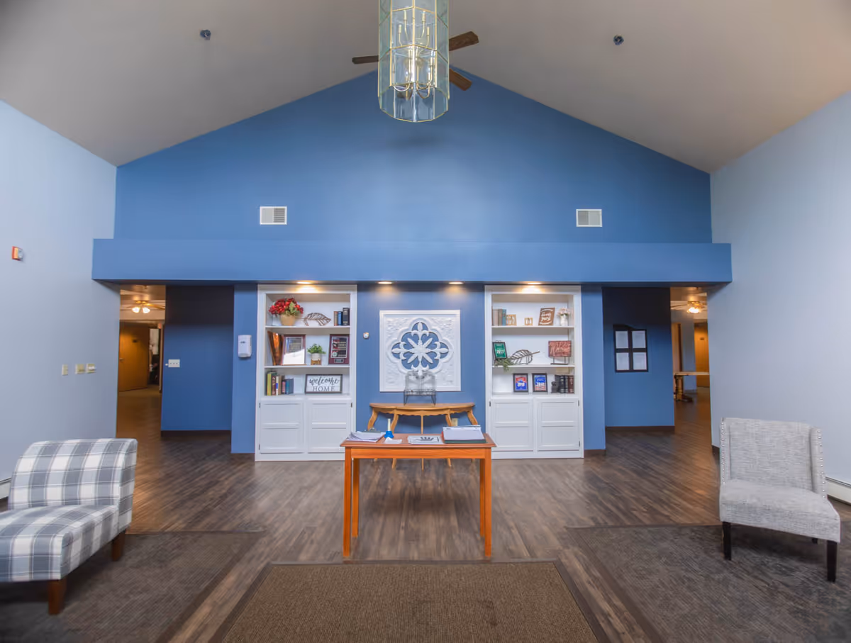 Spacious senior living lobby with a blue accent wall, built-in shelving, a central table, and seating.