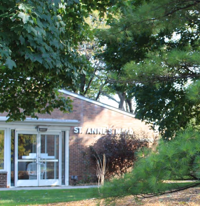 Brick building entrance for St. Anne's Mead partially obscured by trees and landscaping.
