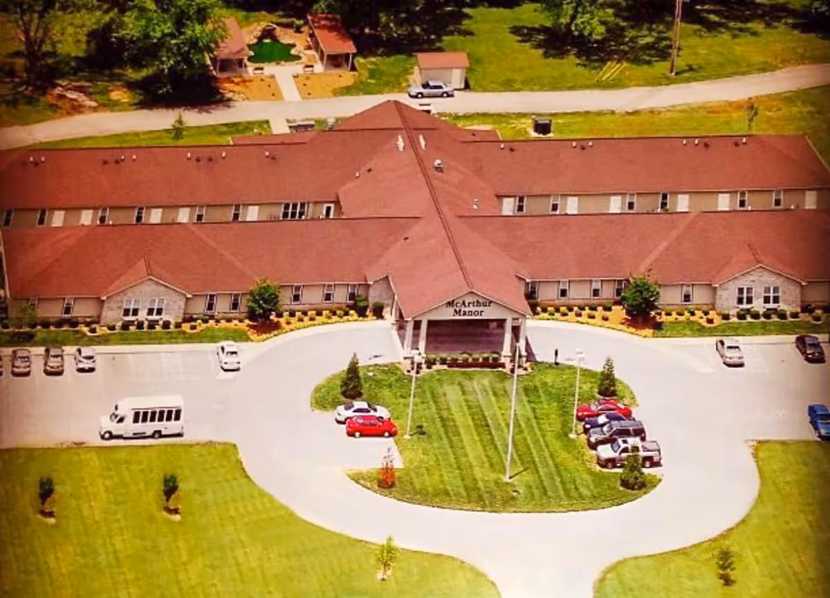 Aerial view of McArthur Manor assisted living building with a circular driveway, front entrance, and parked cars.