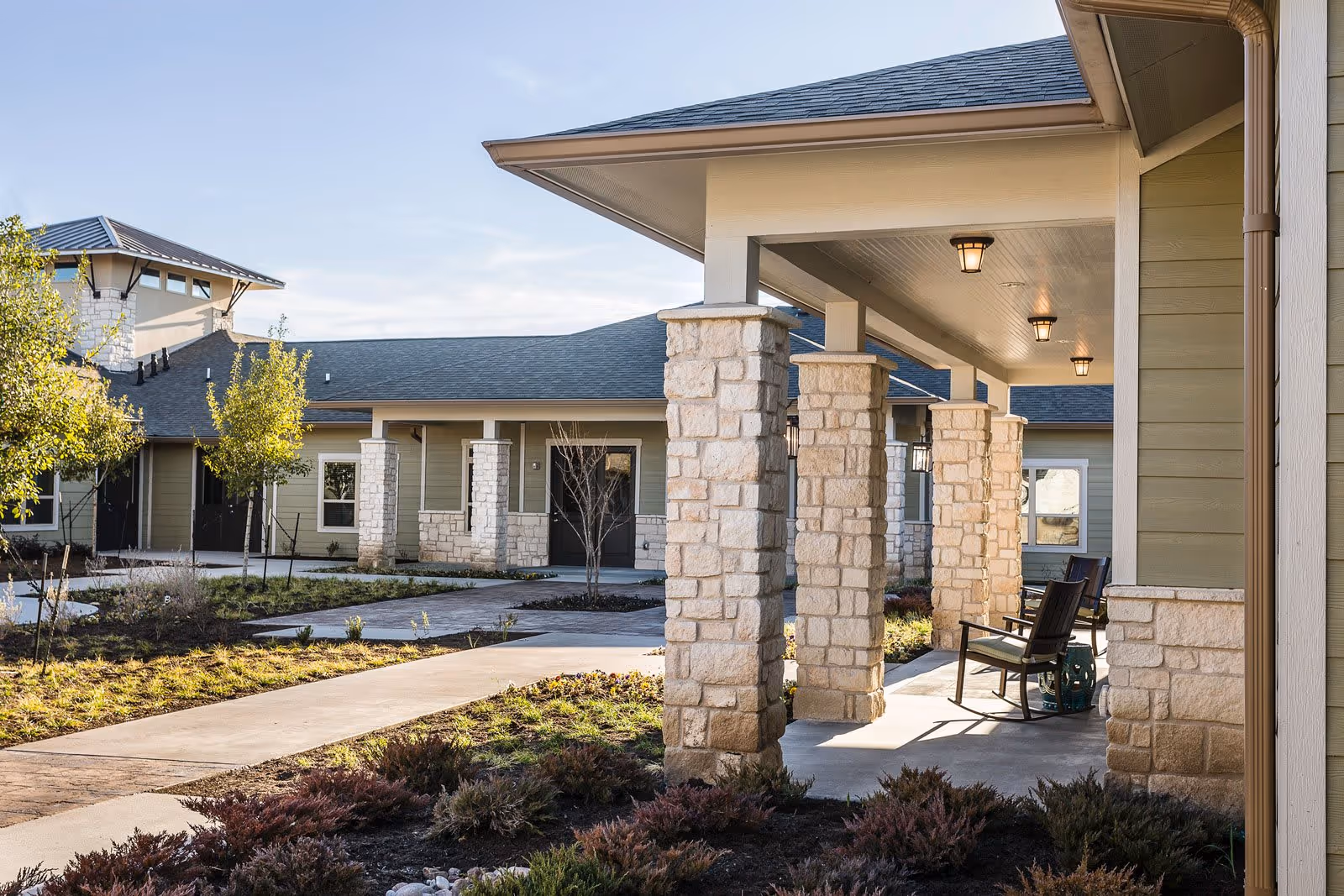 Covered stone-columned porch and walkway leading through a landscaped courtyard at an assisted living facility.