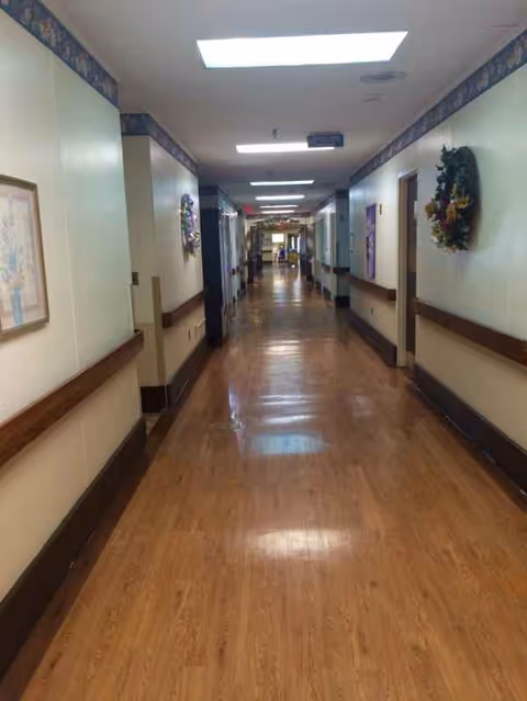 Long, well-lit hallway in a senior living facility with wreath decorations on the walls.