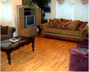 Cozy living room with hardwood floors, a sofa set with patterned pillows, a wooden coffee table and an entertainment cabinet with a TV near windows.