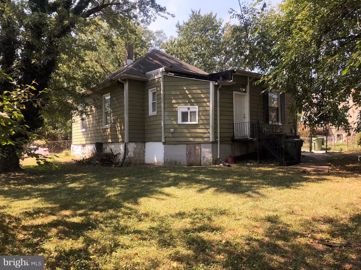 A small single-story green house with a porch and a grassy yard shaded by trees.