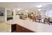 Bright communal dining room with multiple tables and chairs and a service counter in the foreground.